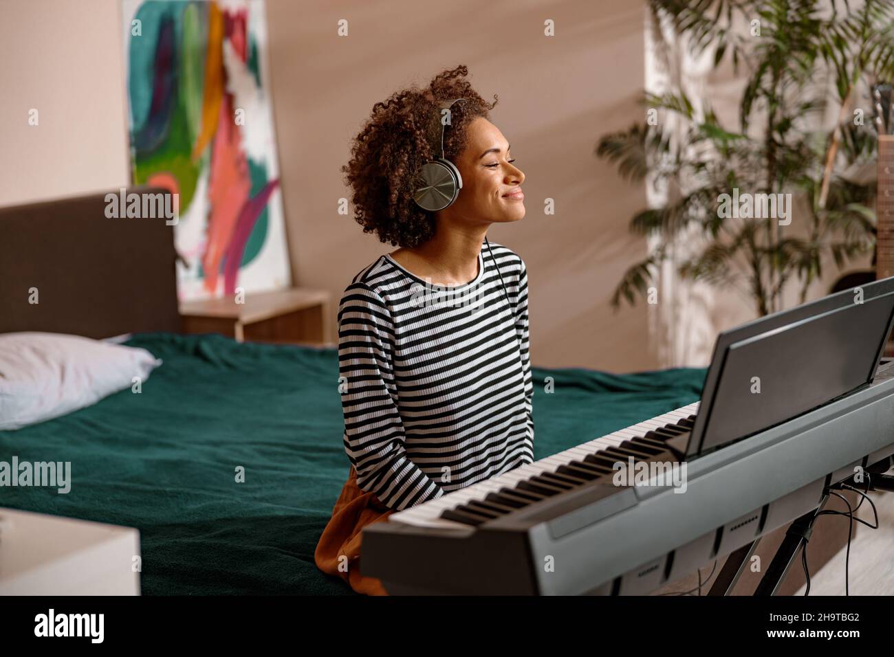 Giovane donna sorridente seduto accanto al sintetizzatore a casa Foto Stock