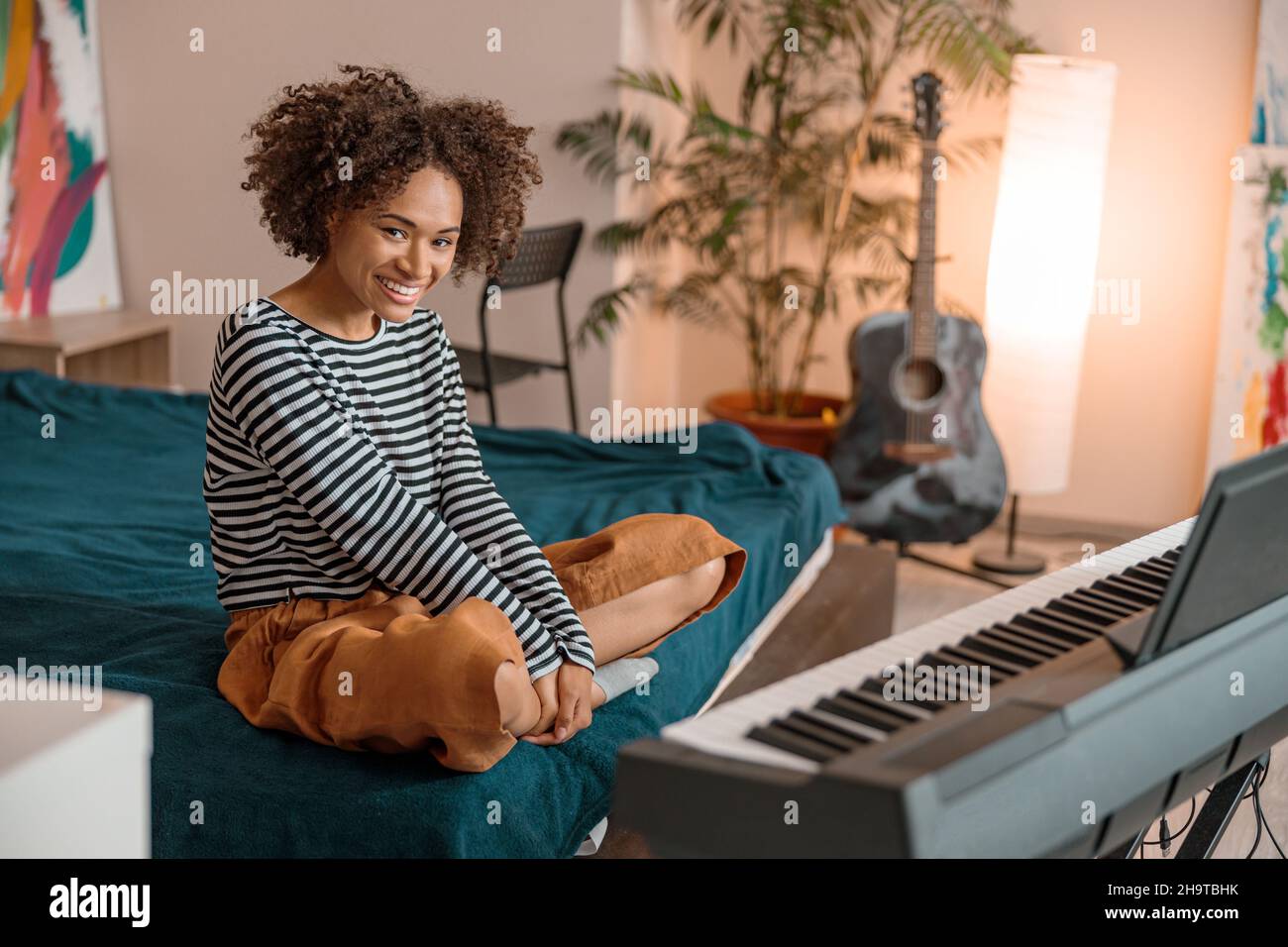 Gioioso musicista femminile seduto vicino al sintetizzatore a casa Foto Stock