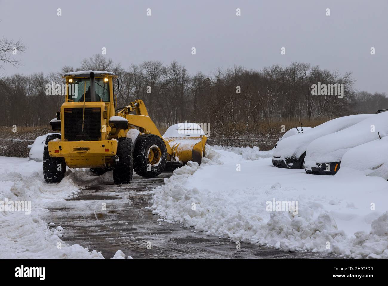 Manutenzione su strada del trattore che rimuove la neve dal parcheggio per l'auto dopo la nevicata Foto Stock
