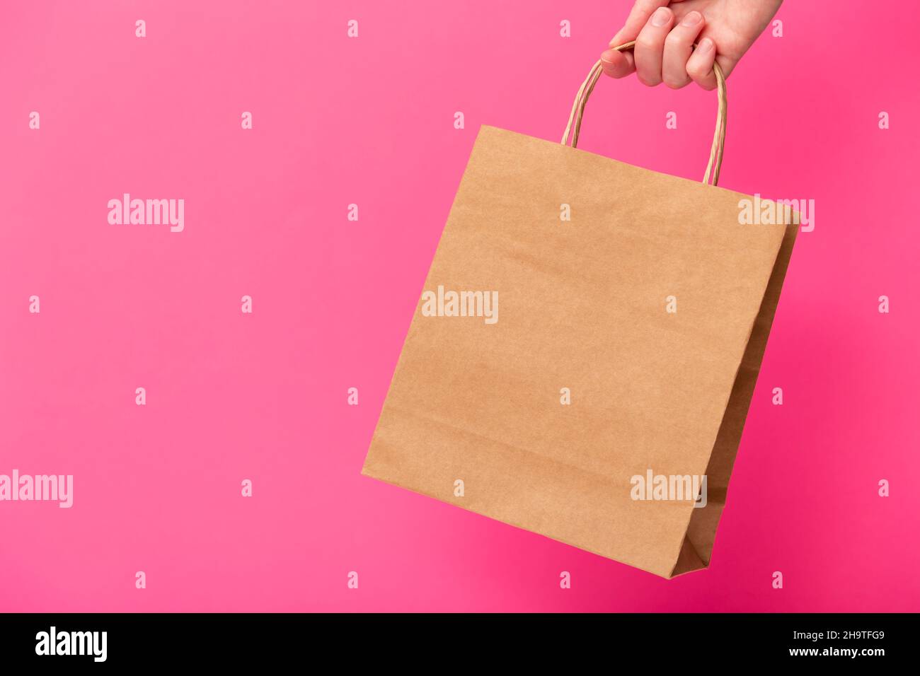 Donna mano che tiene bruno mestiere bianco shopping bag isolato su sfondo rosa. Vendita del black friday, sconto, riciclaggio, shopping e concetto di ecologia Foto Stock
