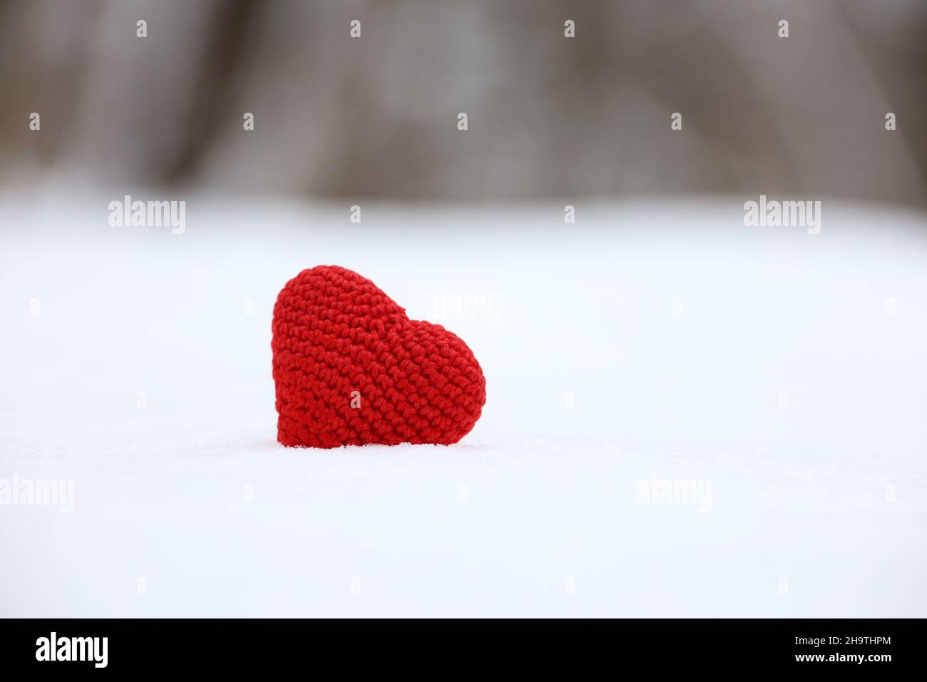 Cuore rosso lavorato a maglia nella neve nella foresta invernale. Carta di San Valentino, simboli d'amore, sfondo per evento romantico, festa di Natale Foto Stock