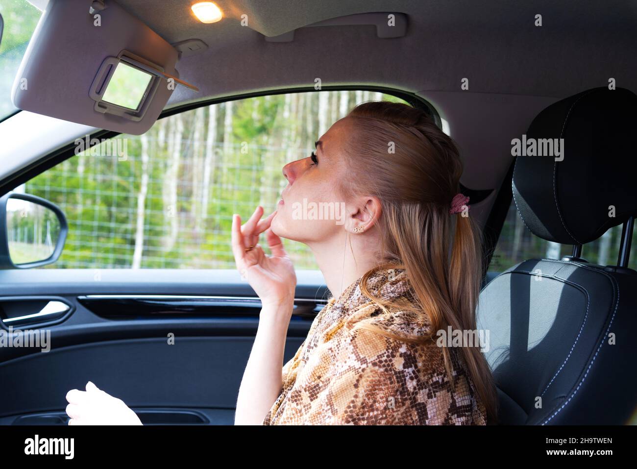 La donna nella vettura sul sedile del passeggero esamina il volto nello specchio. Foto Stock