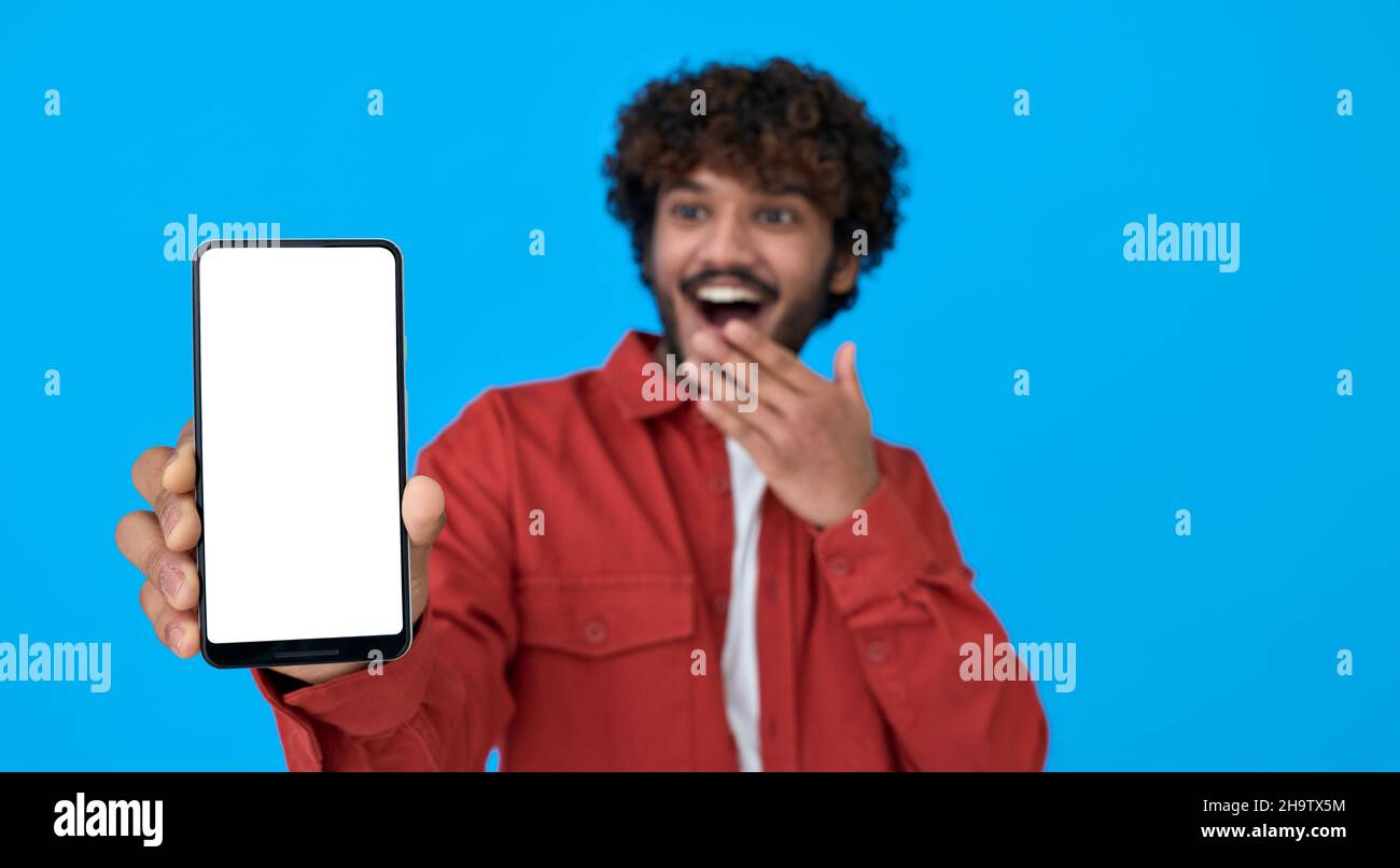 Il giovane indiano eccitato che tiene il telefono che mostra il grande schermo bianco del mockup. Foto Stock