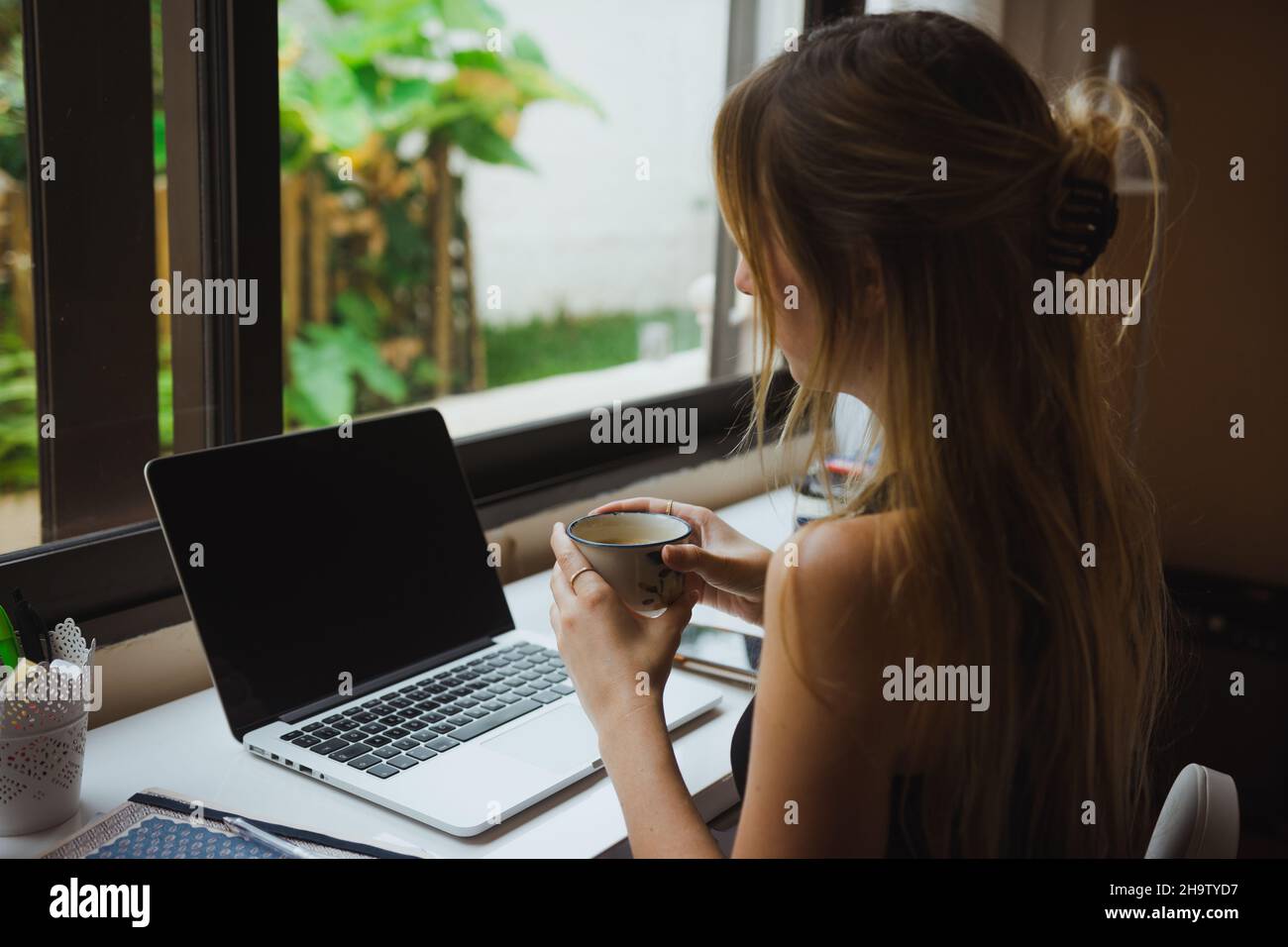 Ragazza che tiene una tazza di caffè, lavorando in linea Foto Stock