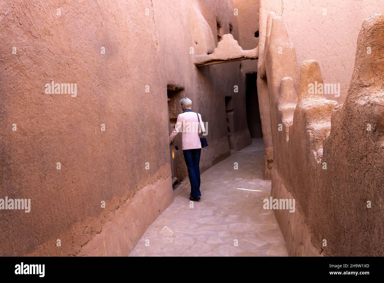 Una sola donna turistica occidentale in piedi nella strada stretta in Ushaiqer Heritage Village, Arabia Saudita. Vista posteriore. Foto Stock