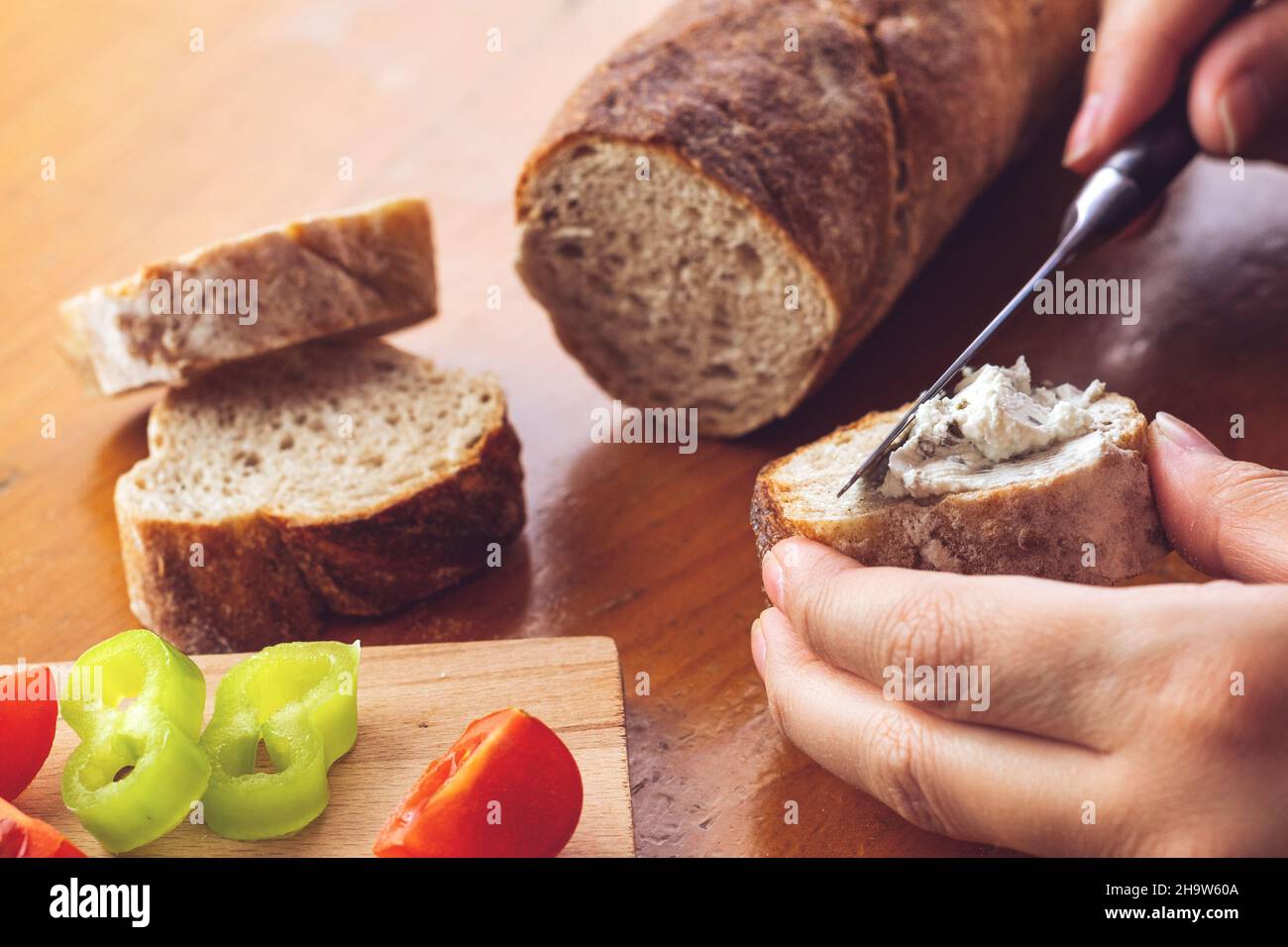 Donna mano spalmando crema di basilico e prezzemolo sul pane con il coltello. Messa a fuoco selettiva. Foto Stock