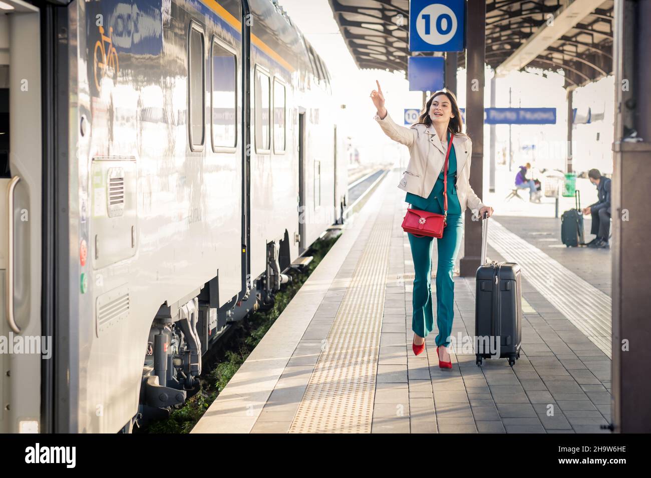 Bella ragazza che corre e insegue il treno in partenza in stazione. Agitando la mano e affrettandosi per ottenere sopra - giovane donna di affari con la valigia che corre Foto Stock