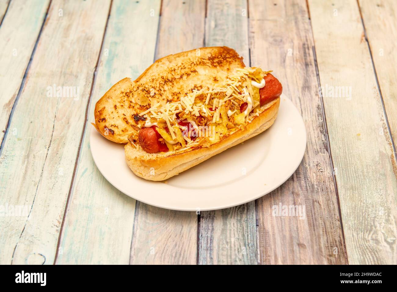 Hot dog speciale con pane brioche con salsiccia, formaggio grattugiato di senape, ketchup e maionese su piatto bianco Foto Stock