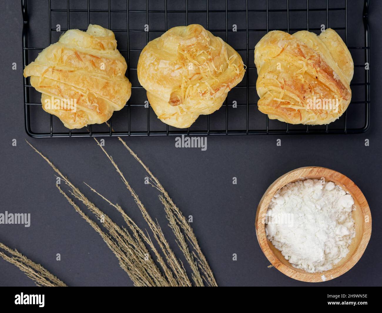 croissant sul grill, con la farina in un recipiente di legno su sfondo nero Foto Stock