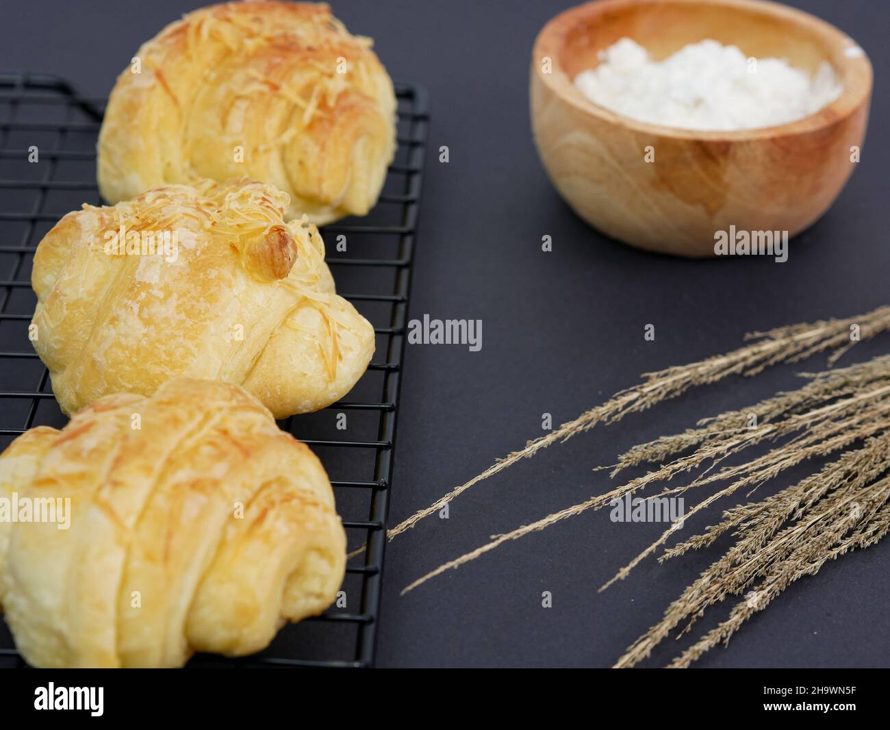 croissant sul grill, con la farina in un recipiente di legno su sfondo nero Foto Stock