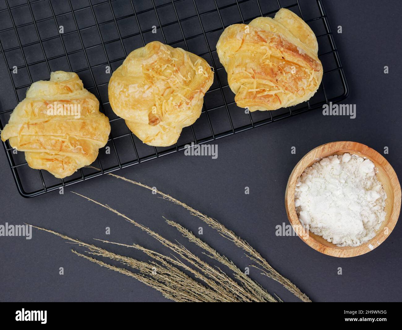 croissant sul grill, con la farina in un recipiente di legno su sfondo nero Foto Stock