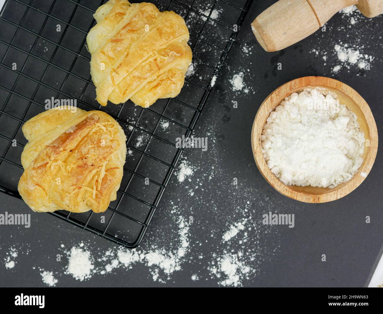 croissant sul grill, con la farina in un recipiente di legno su sfondo nero Foto Stock
