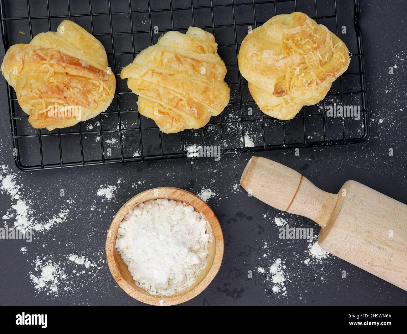 croissant sul grill, con la farina in un recipiente di legno su sfondo nero Foto Stock