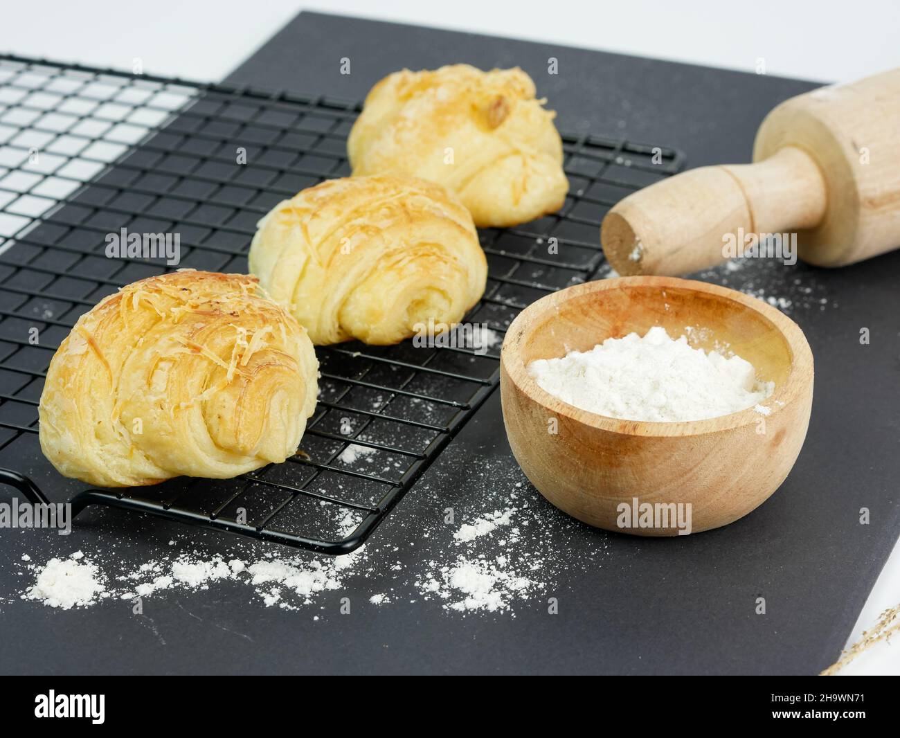 croissant sul grill, con la farina in un recipiente di legno al tavolo Foto Stock