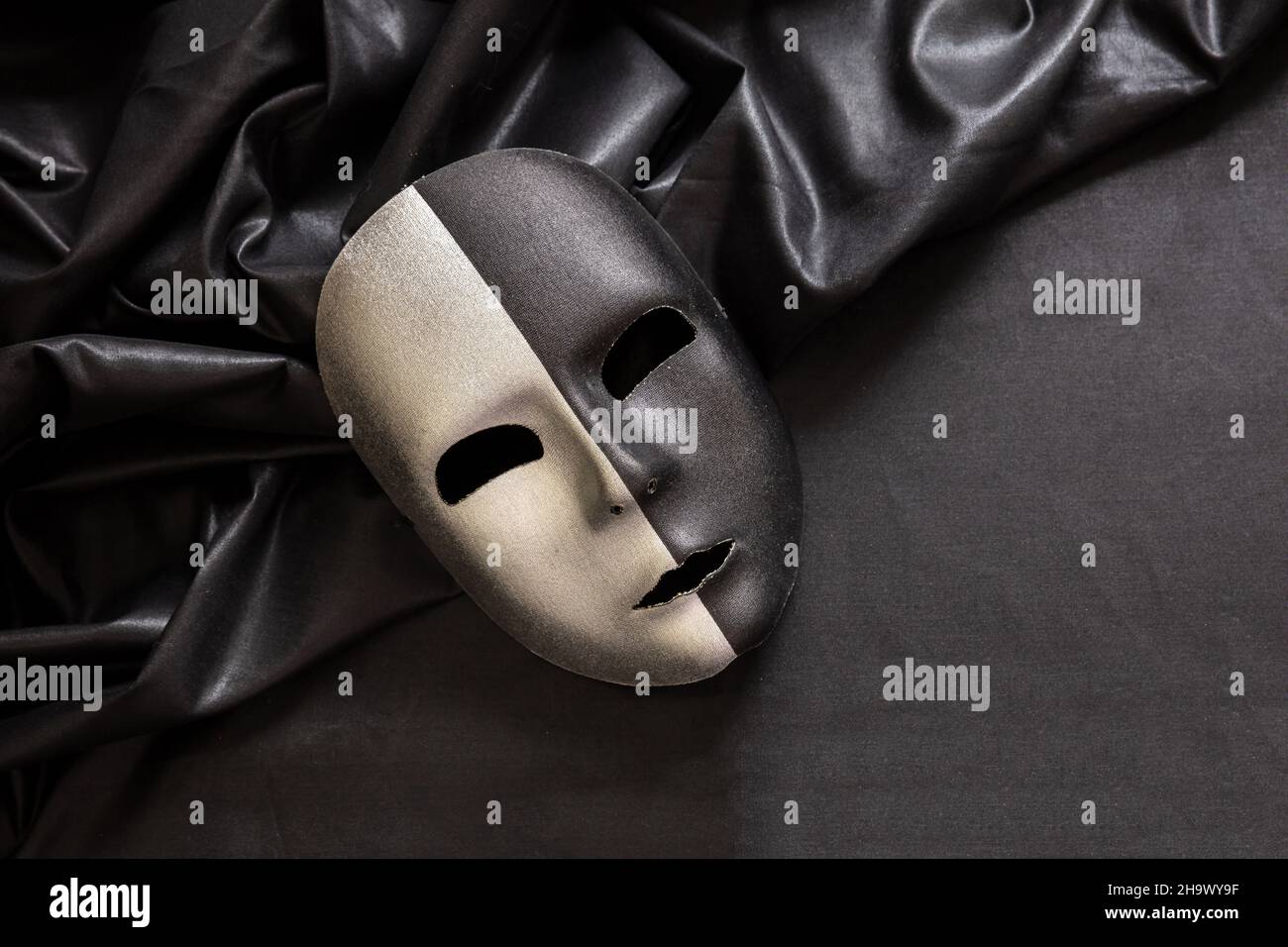 Maschera veneziana a due facce, mezzo nero mezzo argento su sfondo tessile satinato ondulato scuro. Tradizionale festa travestito, Mardi Gras evento masque Foto Stock