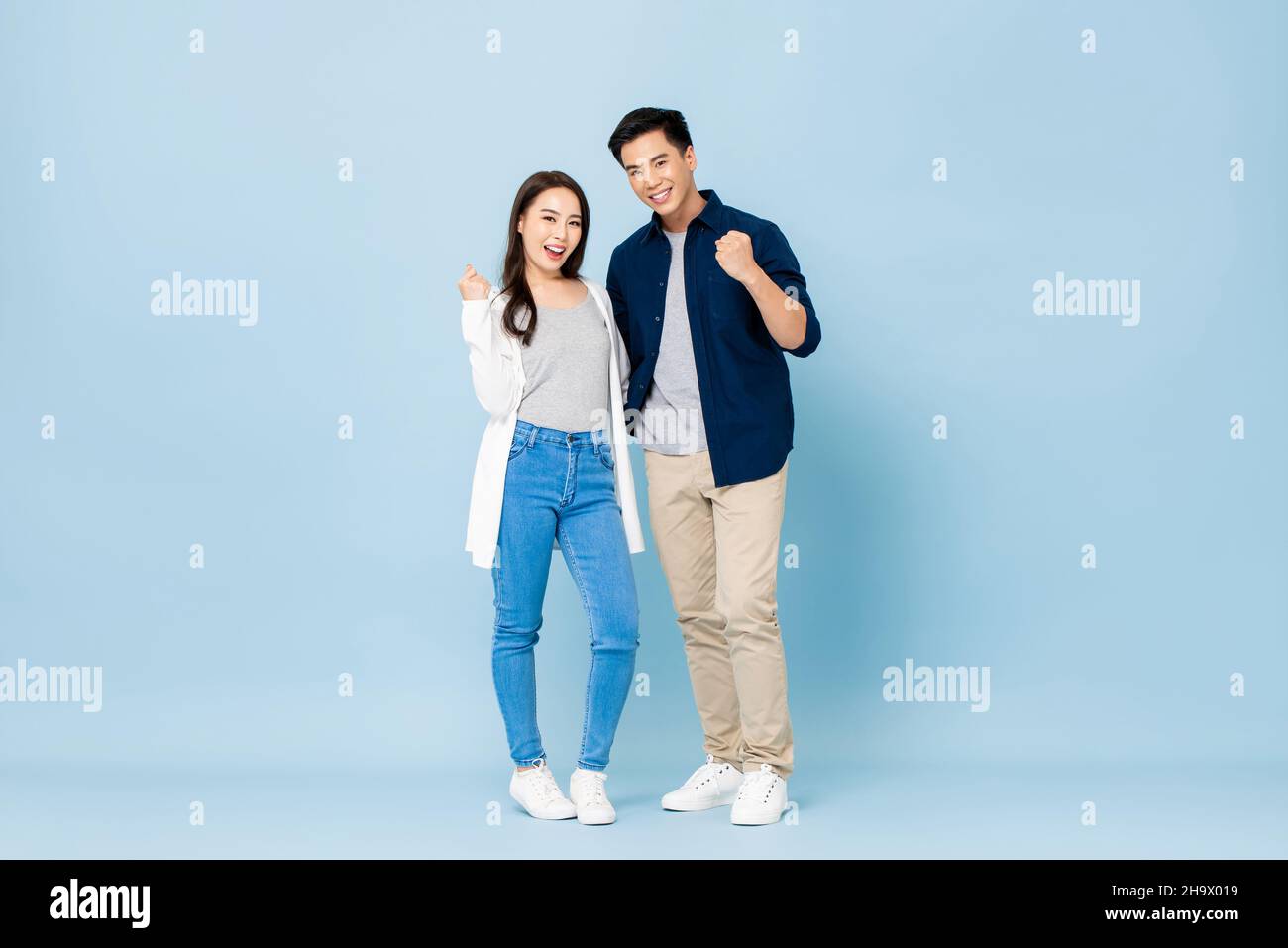 Ritratto completo di giovane coppia asiatica sorridente che si tiene l'un l'altro e pugni clenching in isolato sfondo azzurro studio Foto Stock