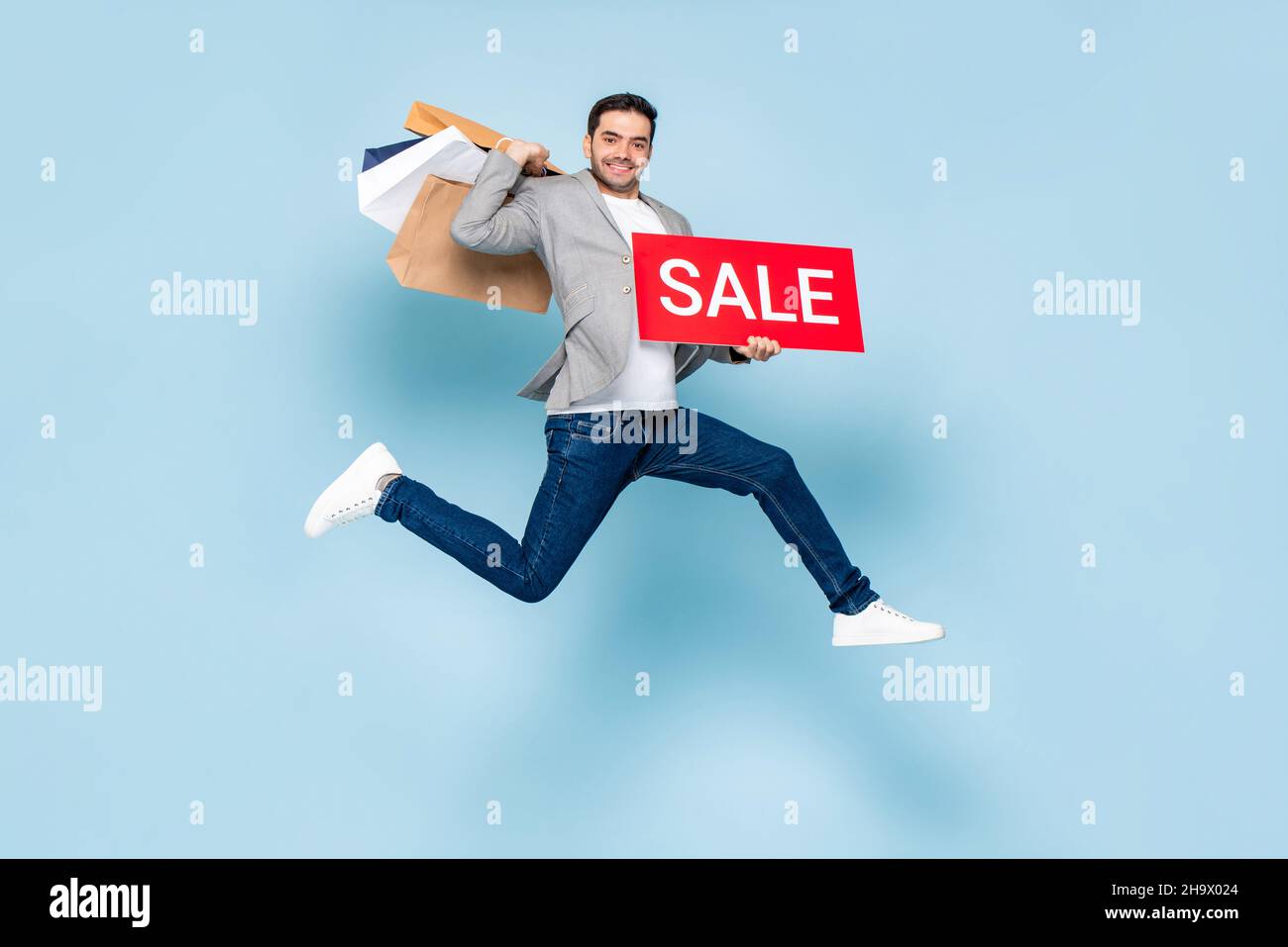 Jumping uomo caucasico hodling rosso vendita segno e shopping borse in blu chiaro isolato sfondo Foto Stock