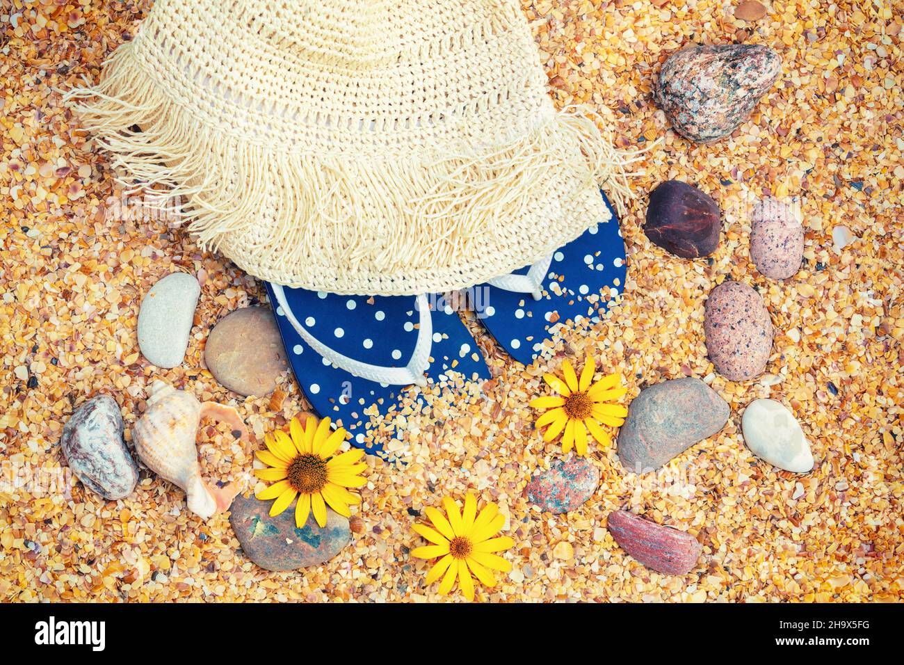 Scena della spiaggia. Cappello di paglia di sole, sandali flip flop e occhiali da sole adagiati sulle conchiglie di cocaina marina sulla spiaggia. Concetto di viaggio Foto Stock