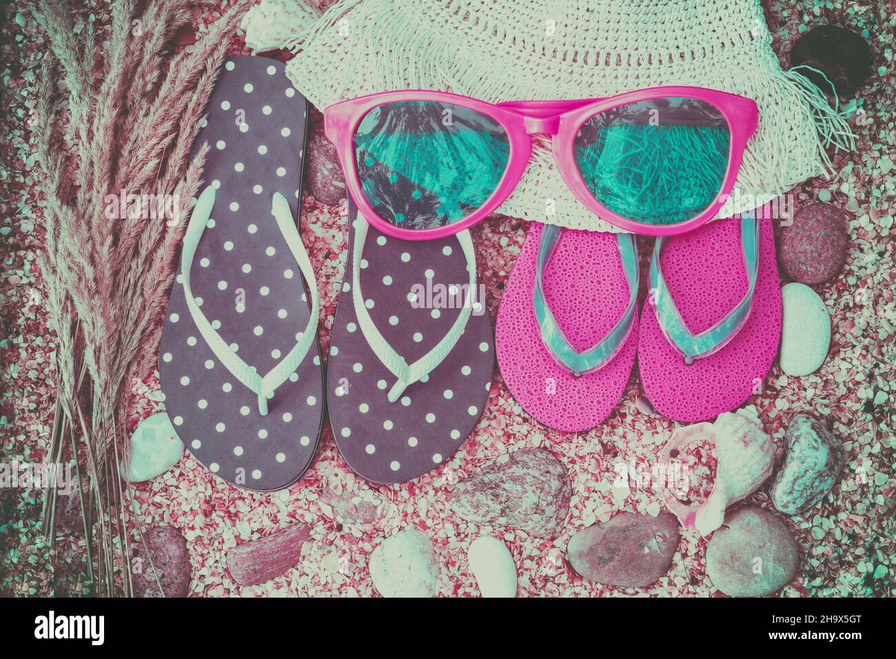 Scena della spiaggia. Cappello di paglia di sole, due paia di sandali flip flop e occhiali da sole adagiati sulle conchiglie di cocaina marina sulla spiaggia. Concetto di vacanza Foto Stock