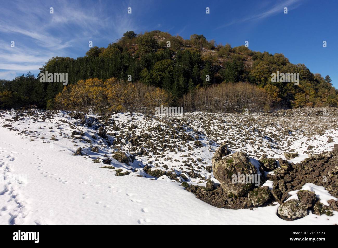 Tempo e stagione in Sicilia il paesaggio montano di vecchie rocce laviche innevate circonda un antico cono vulcanico boscoso nel Parco dell'Etna Foto Stock