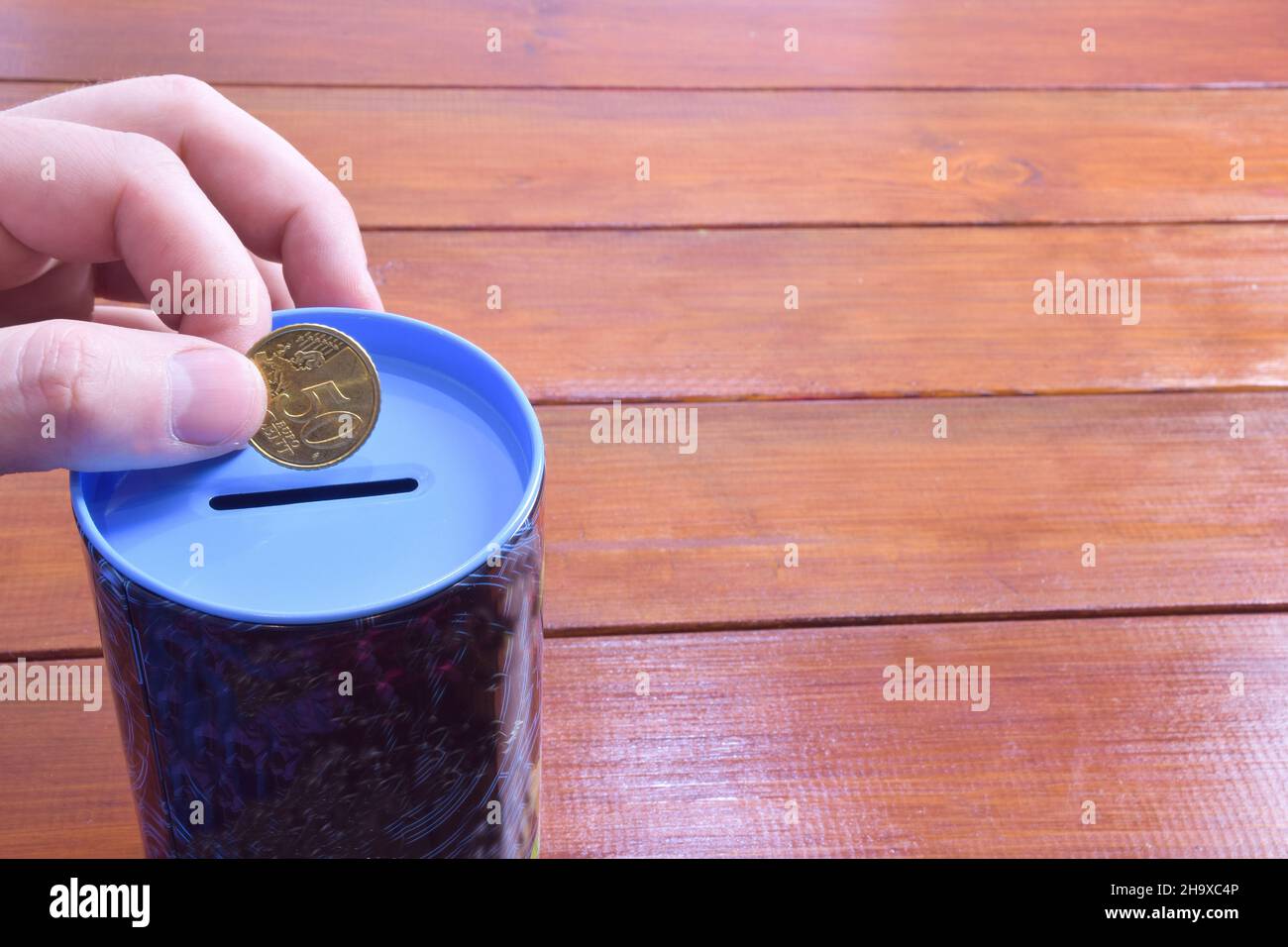 Una mano tiene 50 centesimi di euro su una banca di maialino su un fondo di legno. A destra c'è uno spazio vuoto per l'etichettatura o l'inserimento Foto Stock