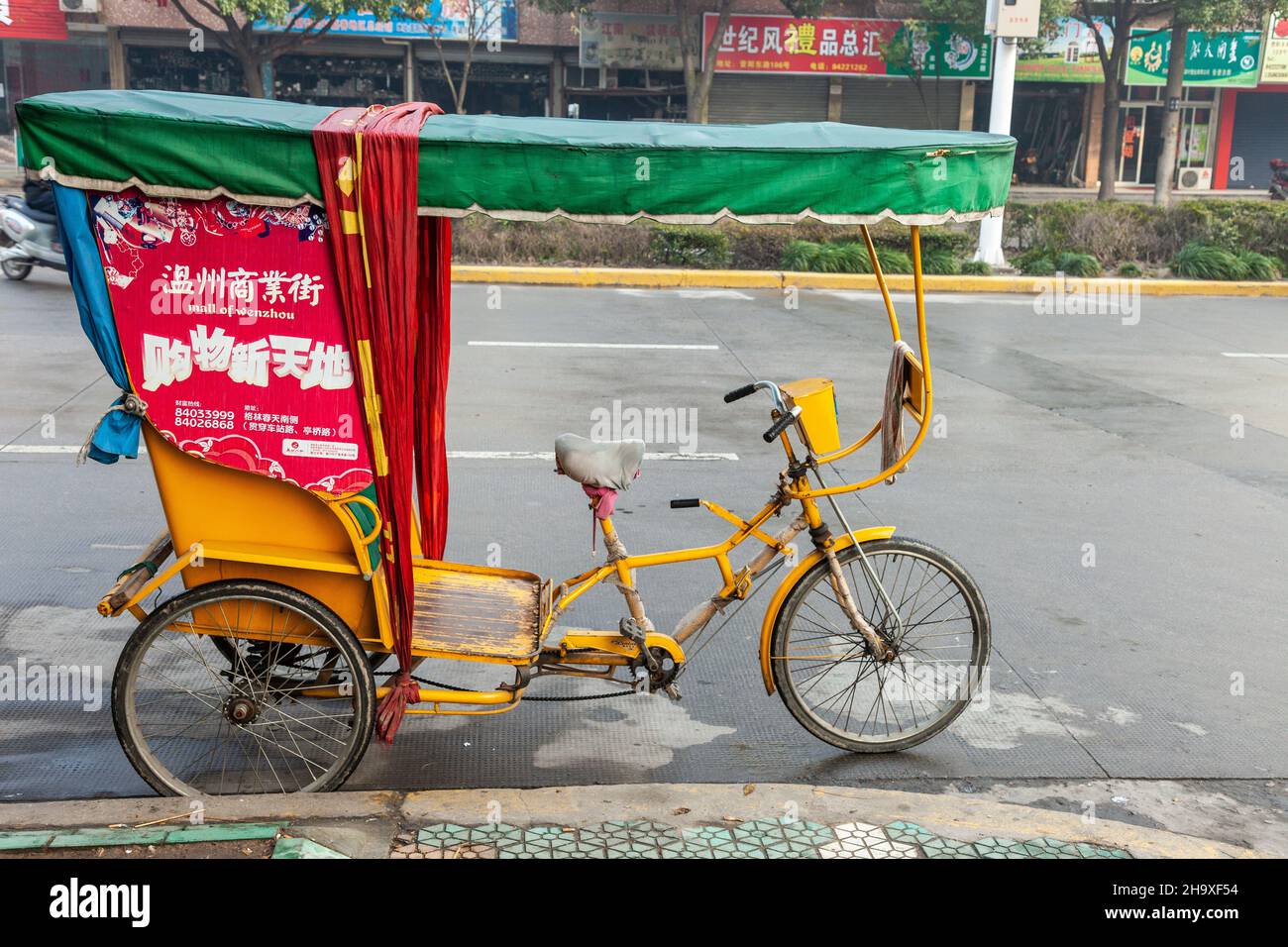 Risciò giallo adornato di pubblicità, parcheggiato in una strada a Jiashan, Cina Foto Stock