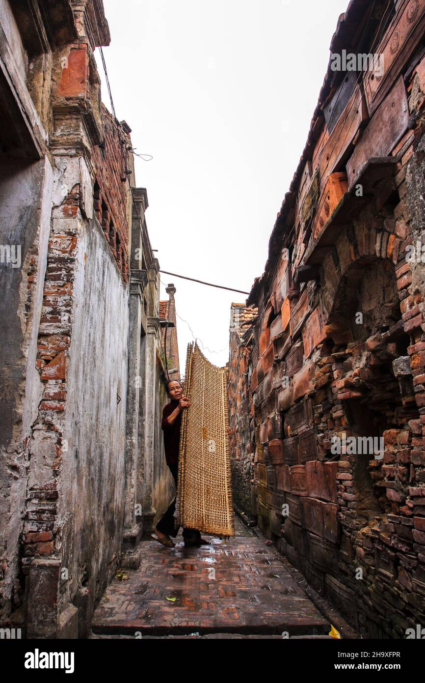 Una donna porta un vassoio di carta di riso per asciugare al sole in un piccolo vicolo nel villaggio di Tho ha, Bac Giang, Vietnam Foto Stock