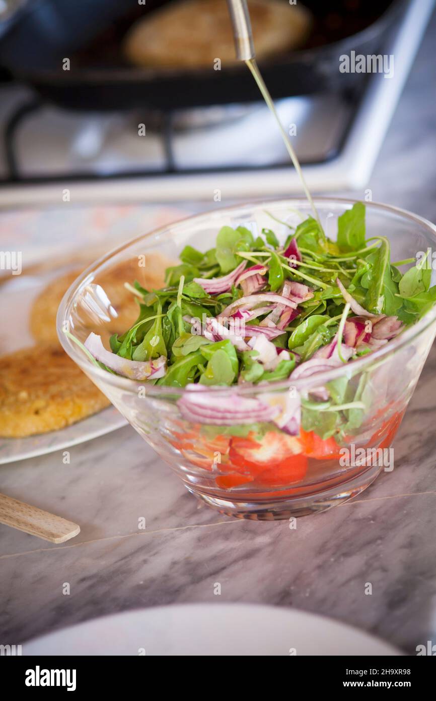 Insalata verde con cipolle rosse e pomodori che vengono conditi con olio d'oliva Foto Stock