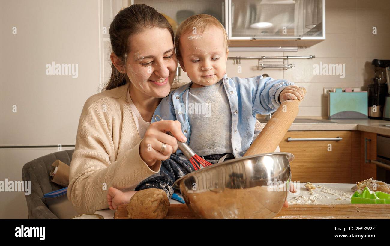 Bambino piccolo che aiuta la madre impastando l'impasto e tenendo la spina per cuocere il pane in cucina. Concetto di piccolo chef, i bambini che cucinano cibo Foto Stock