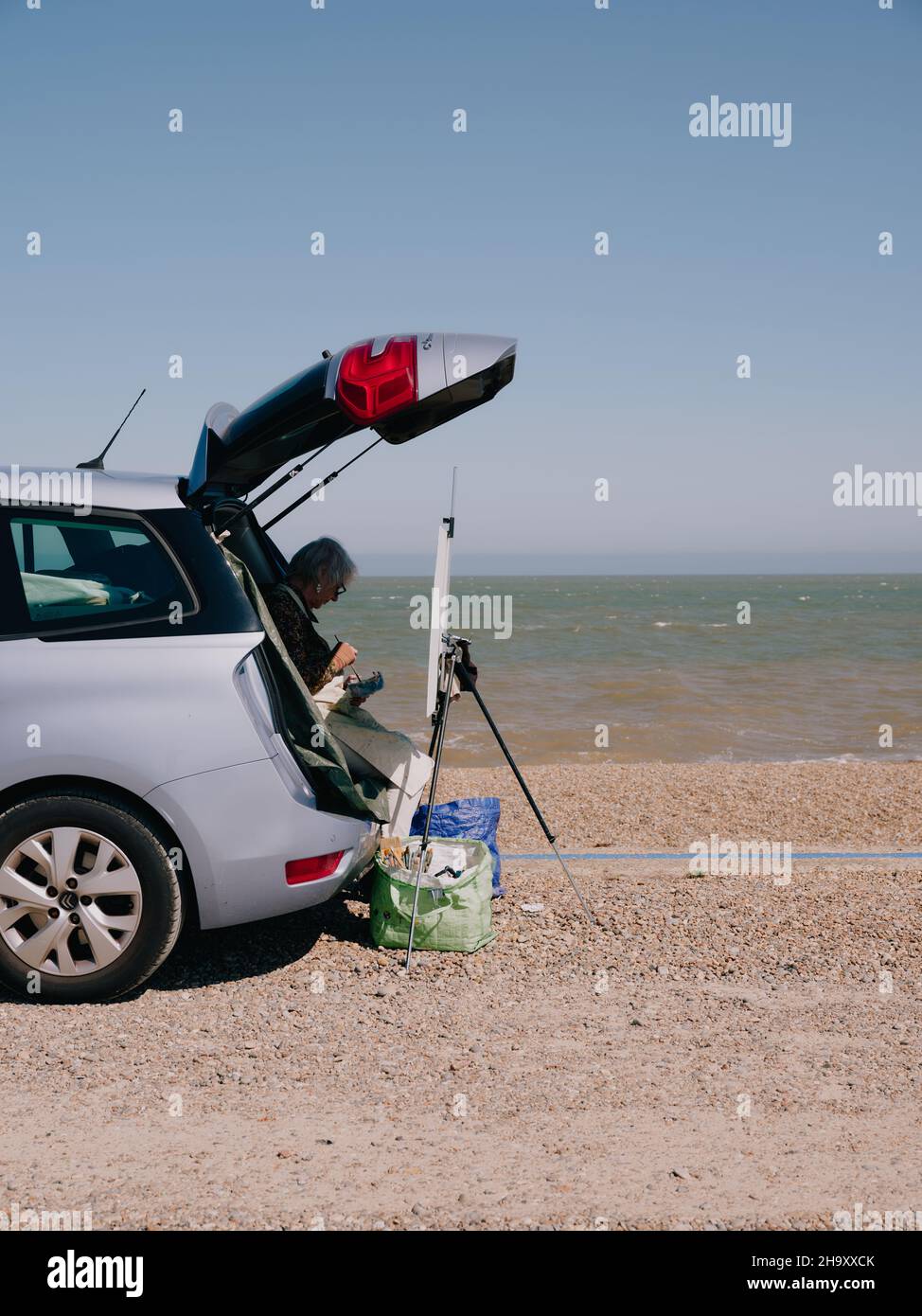 Un artista dipinge dal bagagliaio della loro auto con un cavalletto e tela sulla costa estiva del mare del Regno Unito - pittura ad aria plein - en plein air Foto Stock