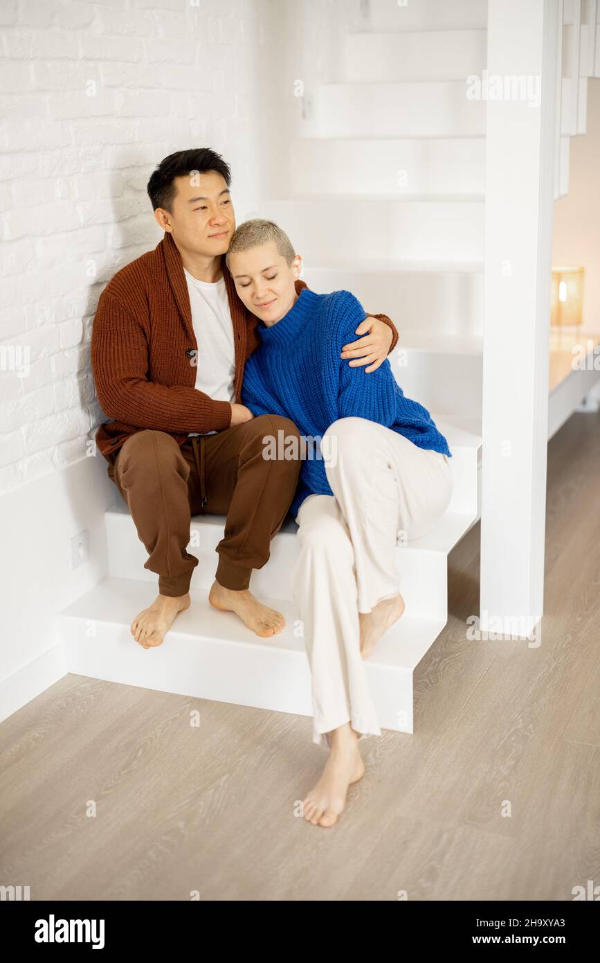 Uomo asiatico abbraccia moglie caucasica sulle scale a casa Foto Stock