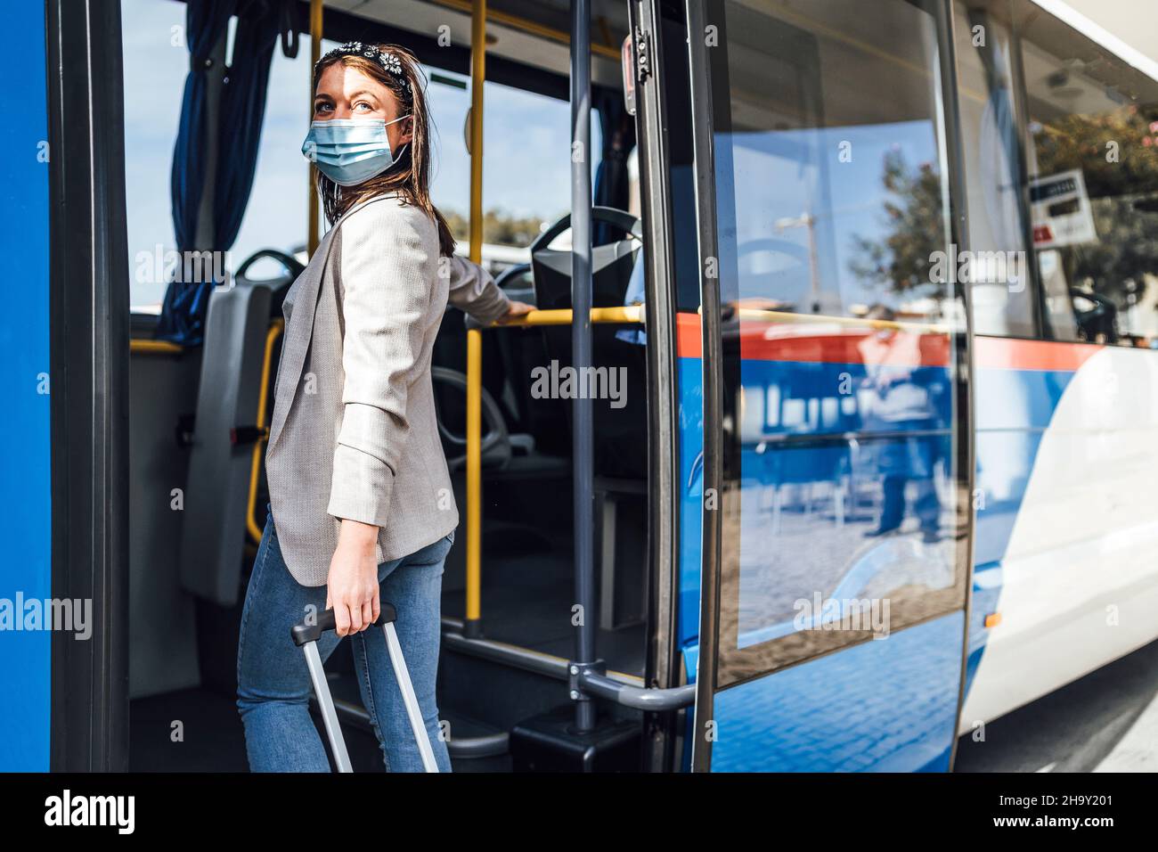 Giovane donna con bagaglio e maschera di protezione imbarco per l'autobus di Faro, Portogallo Foto Stock