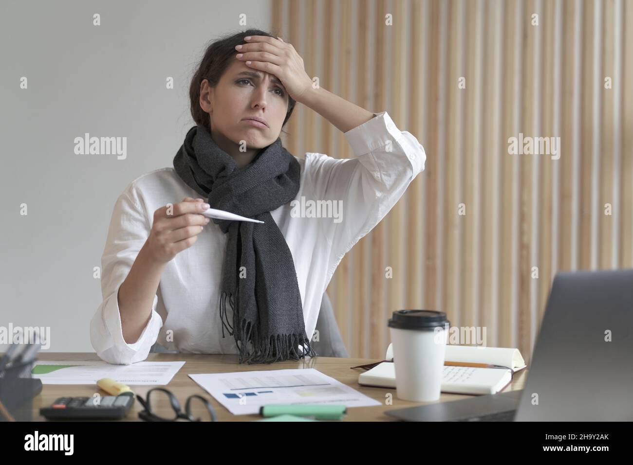 Malsano giovane donna europea che lavora in ufficio con termometro digitale e fronte toccante Foto Stock