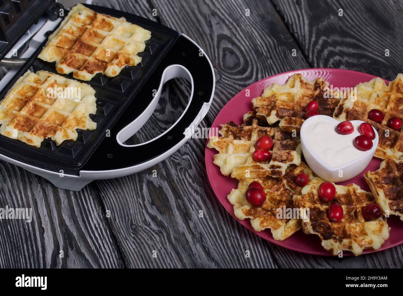 Waffle con panna acida e mirtilli. Sdraiati su un piatto. Accanto all'hotel c'è una macchina per preparare i waffle. Su assi di pino nero. Foto Stock