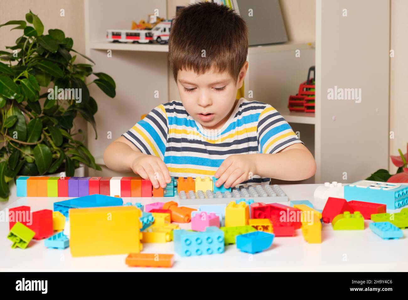 Un ragazzo di 4 anni in una T-shirt a righe gioca con mattoni multicolore del costruttore. Giochi educativi per bambini. Per un negozio di giocattoli Foto Stock
