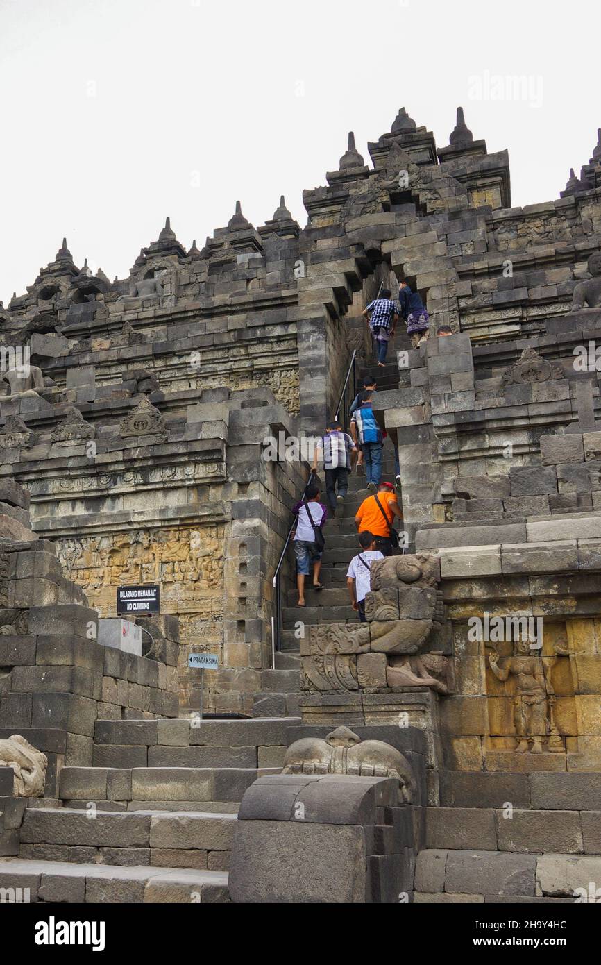 Persone che camminano su scale attraverso archi per accedere alle terrazze superiori presso l'antico Tempio Borobudur. Popolare meta turistica e buddista di pellegrinaggio. Foto Stock