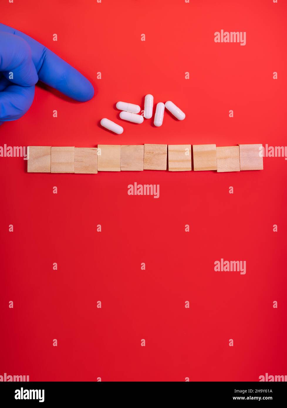 Le mani nei guanti medici puntano su blocchi di legno su sfondo rosso colorato con pillole di medicina. Il concept book copre la temperatura medica scientifica o biologica Foto Stock