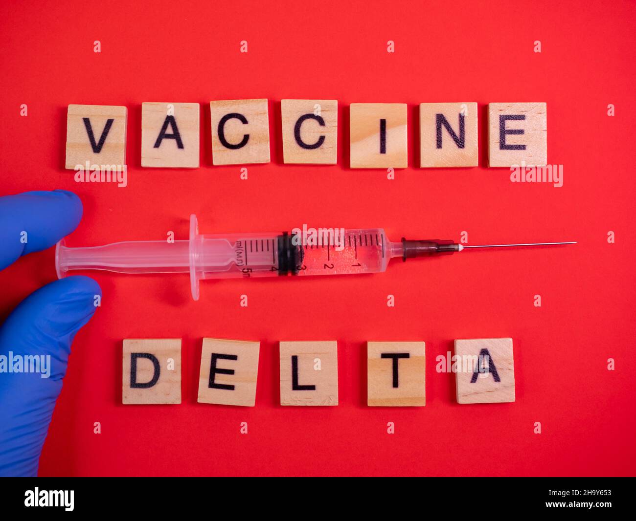 La variante Omicron sposta Delta. Comparsa di nuovo ceppo pericoloso di coronavirus COVID-19 Omicron. Guanti per mani. Parole vaccino delta su colorato rosso ba Foto Stock