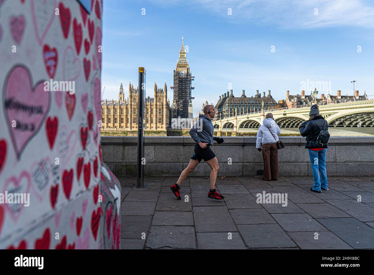 WESTMINSTER LONDRA, REGNO UNITO. 9 dicembre 2021. Un uomo che corre davanti ai cuori dipinti al muro commemorativo nazionale di Covid lungo il lungofiume del Tamigi. il primo ministro Boris Johnson ha annunciato restrizioni più severe del piano B Covid durante un discorso televisivo da Downing Street il mercoledì sera, tra cui il lavoro da casa, indossare maschere e introdurre i passi Covid per combattere l'ascesa esponenziale della variante omicron alla luce dello scandalo del partito di Natale a Downing Street. Credit: amer Ghazzal/Alamy Live News Foto Stock