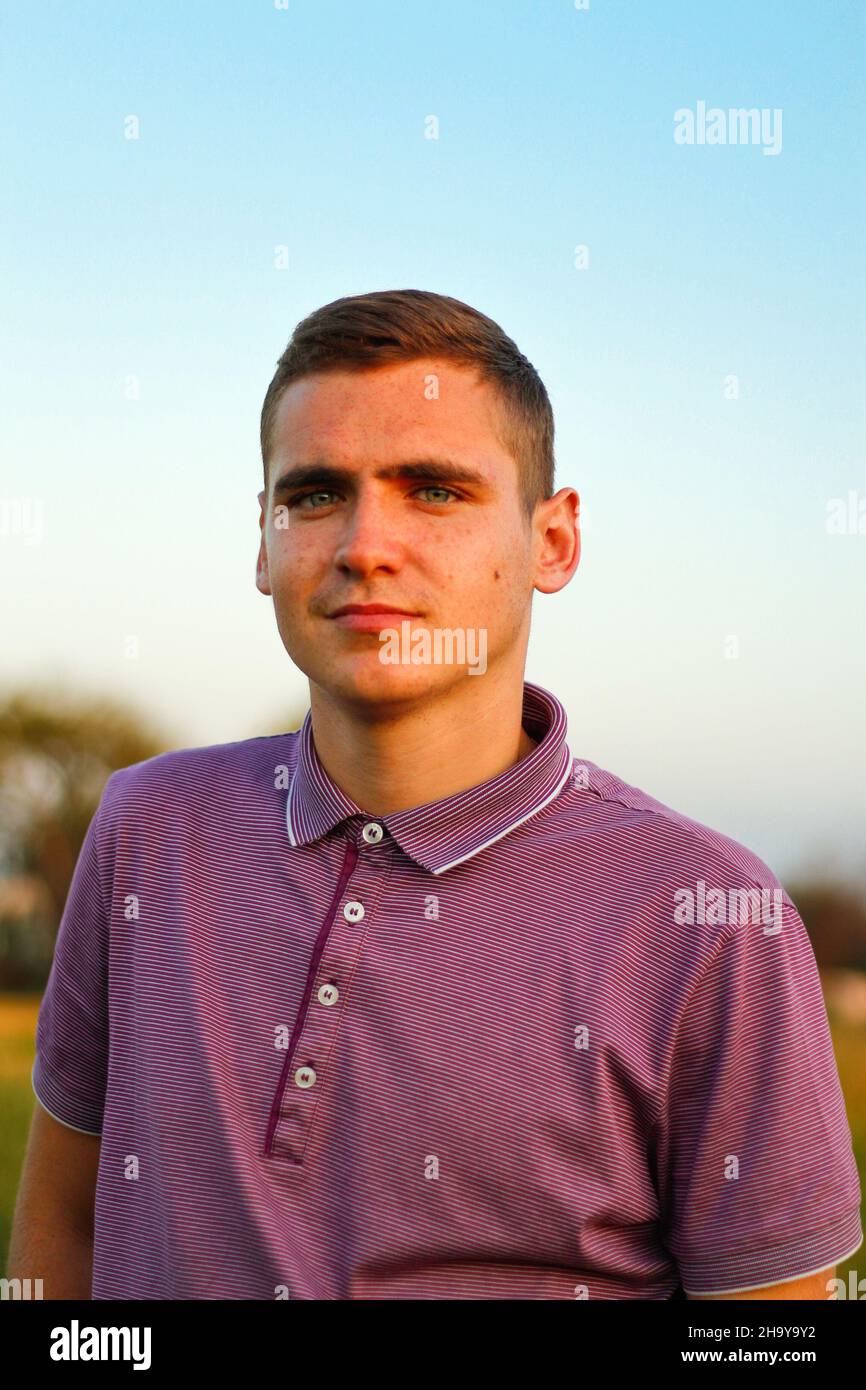 Young People.Portrait di uomo bruna giovane e serio in polo viola in piedi all'aperto sulla natura sfondo al giorno d'estate. 20s anni ragazzo. Millenni Foto Stock