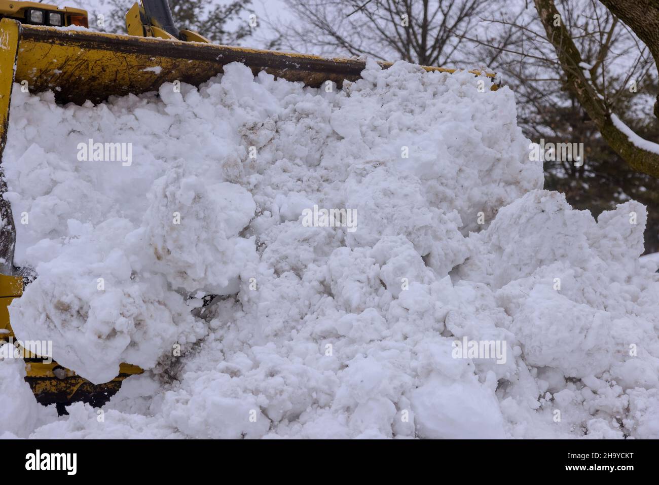 Il trattore giallo pulisce la strada nella neve Foto Stock