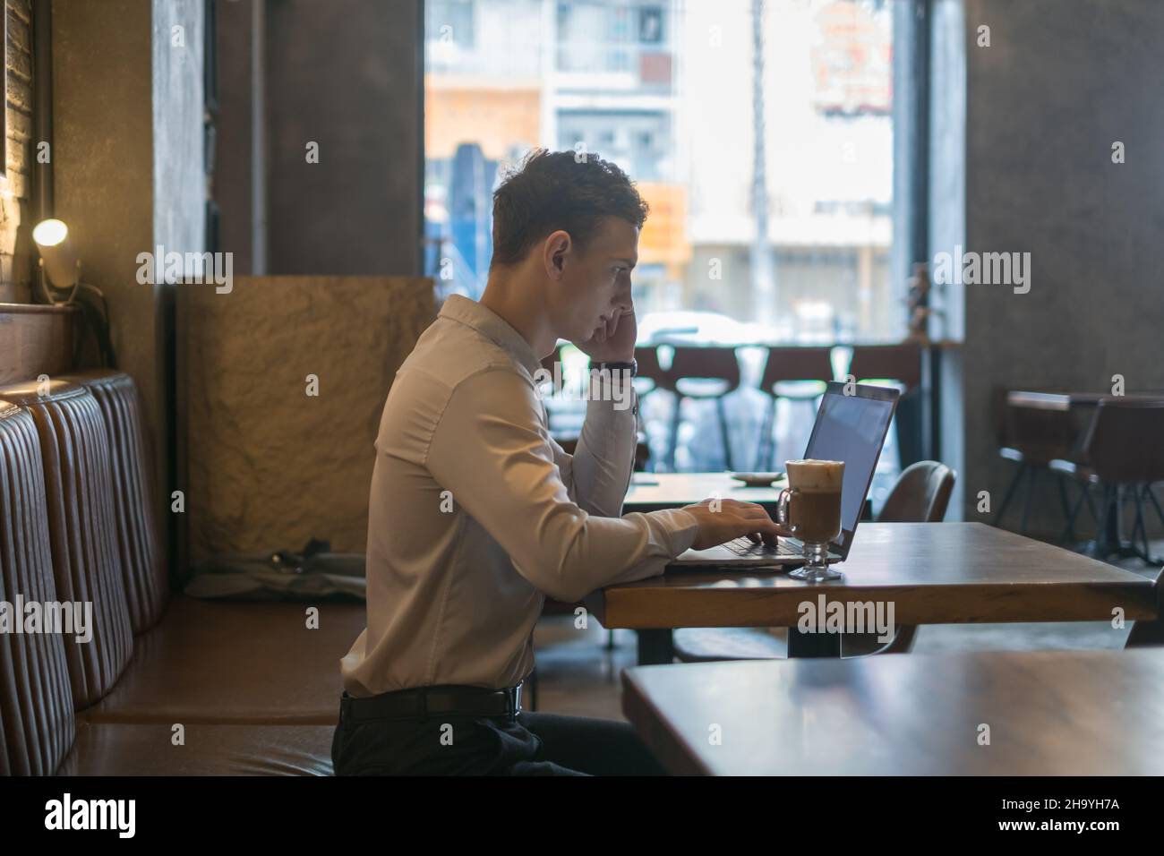 Freelance che lavora in caffetteria con un computer portatile. Pensare, risolvere problemi, nuove idee. Giovane uomo d'affari che naviga in rete su un computer portatile in un bar. Foto Stock