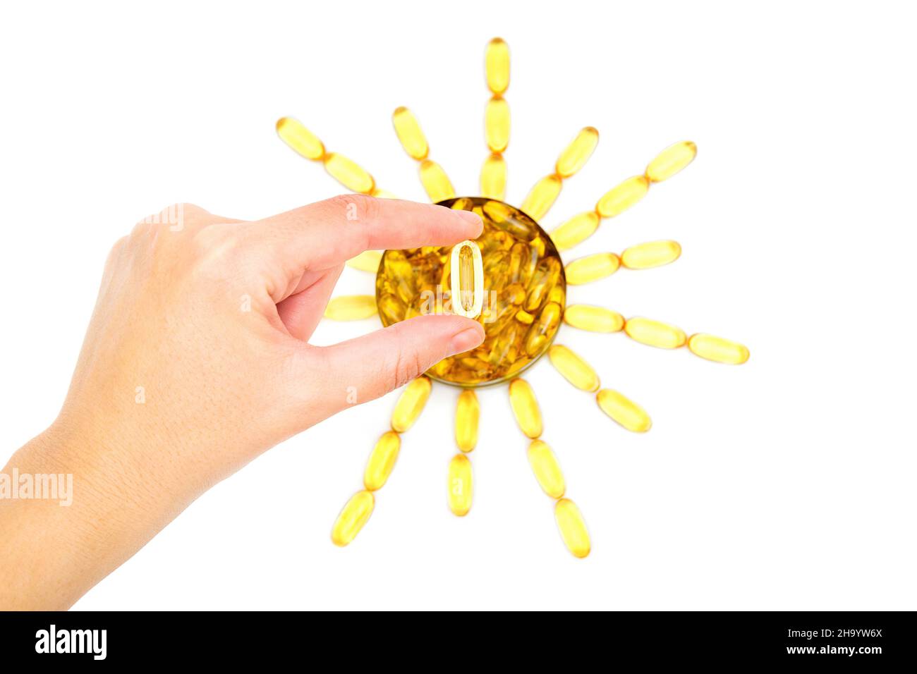 Mano che tiene una pillola di olio di pesce sopra una forma di sole fatta da capsule di softgel di omega-3 su bianco. Foto Stock