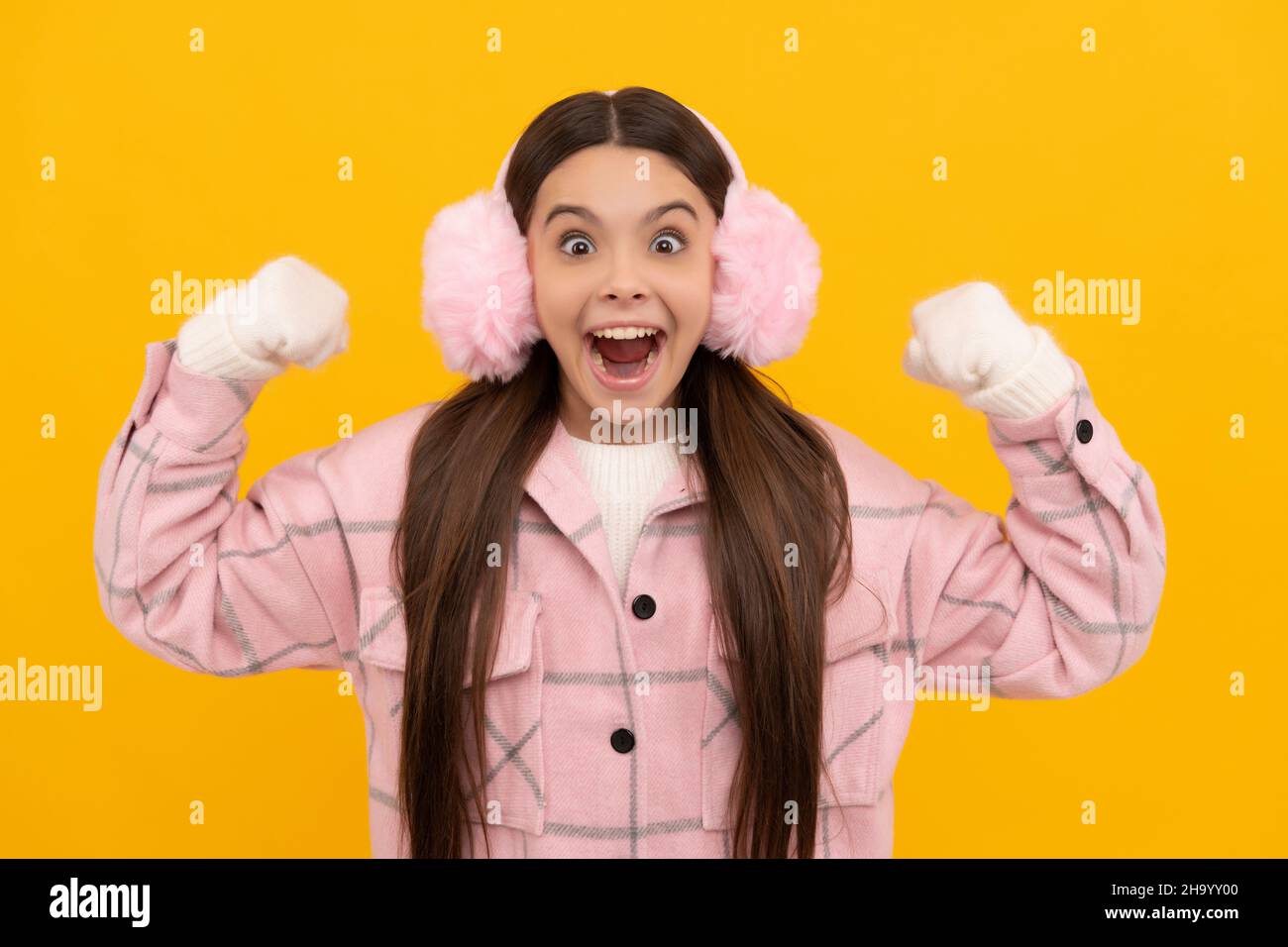 capretto stupito in guanti invernali e cuffie su sfondo giallo, moda invernale Foto Stock