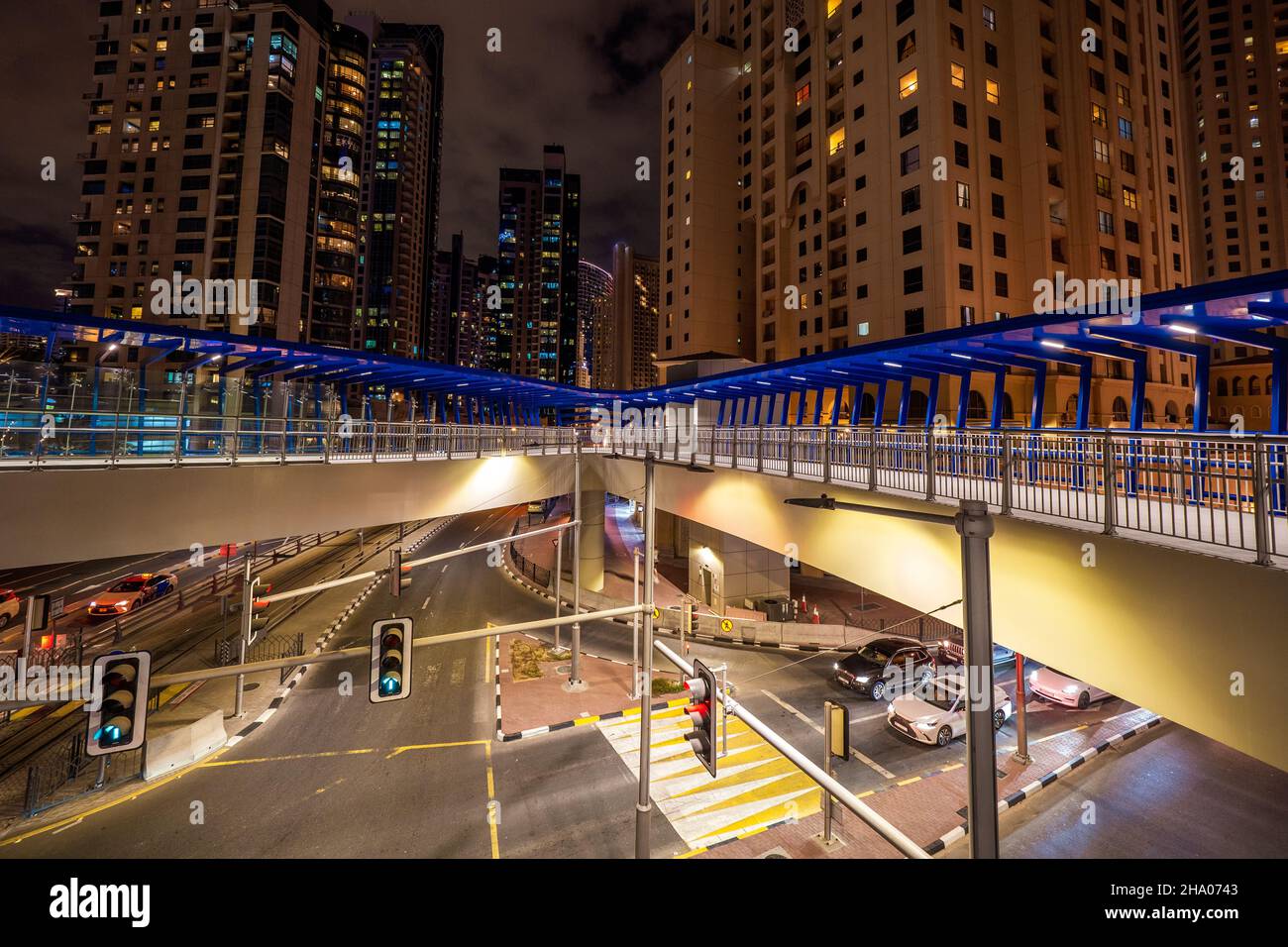 Vista notturna di un grande ponte pedonale attraverso una strada principale nel quartiere di Dubai Marina, Dubai, Emirati Arabi Uniti, circondato da grattacieli Foto Stock