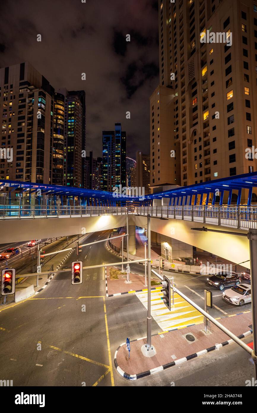 Vista notturna di un grande ponte pedonale attraverso una strada principale nel quartiere di Dubai Marina, Dubai, Emirati Arabi Uniti, circondato da grattacieli Foto Stock