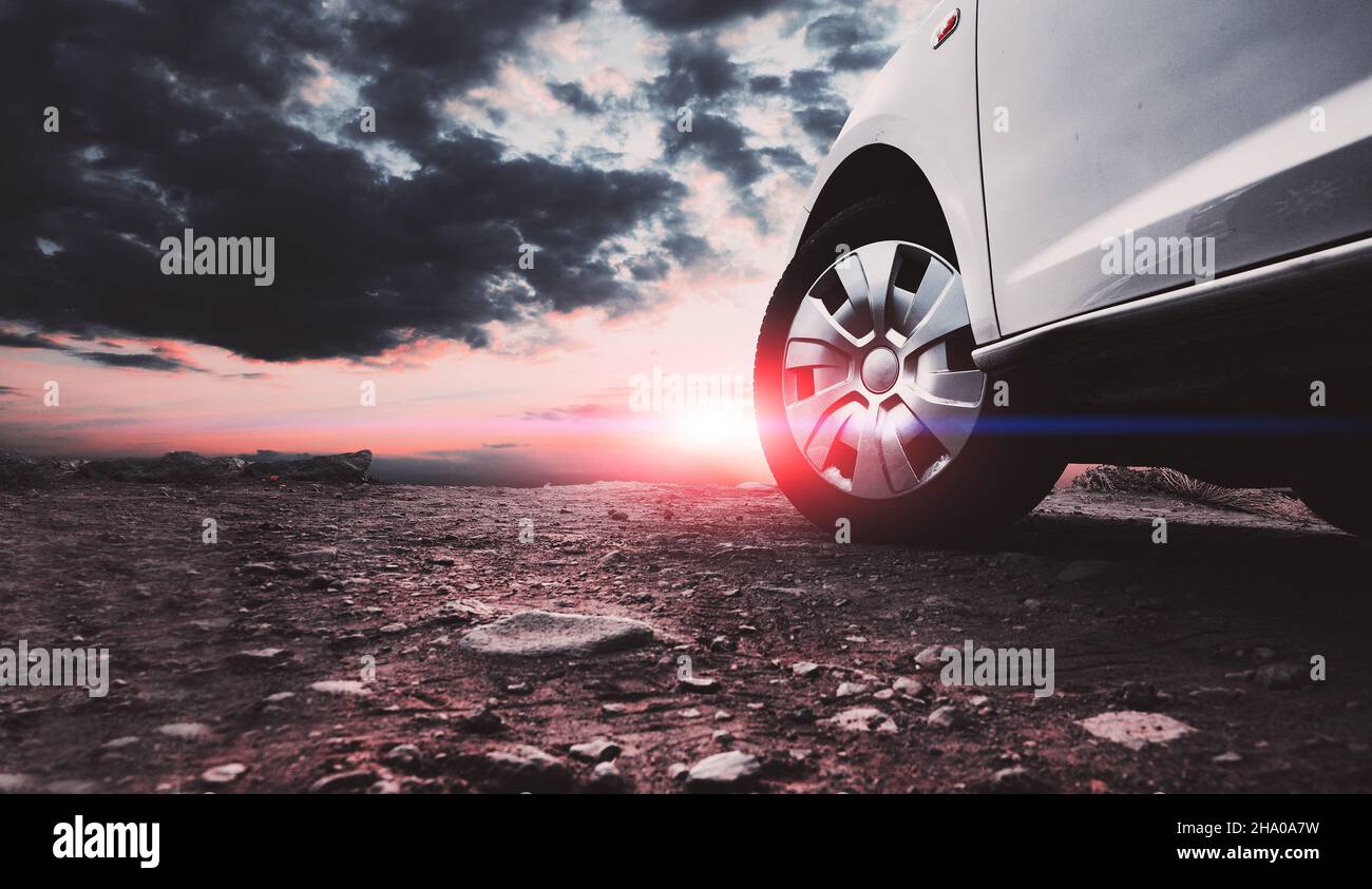 Immagine chiusa di ruote e pneumatici per auto a terra e cielo al tramonto. Viaggio in auto e avventura. Foto Stock