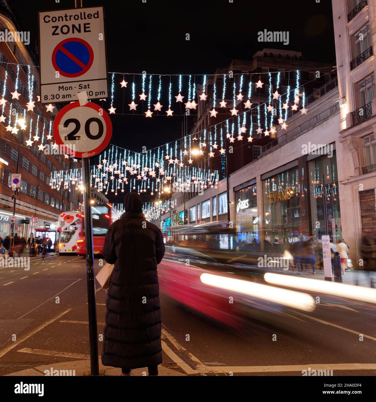 Londra, Greater London, Inghilterra, dicembre 04 2021: Lady si trova a Oxford Street mentre il traffico sibila di notte con le luci di Natale in mostra. Foto Stock