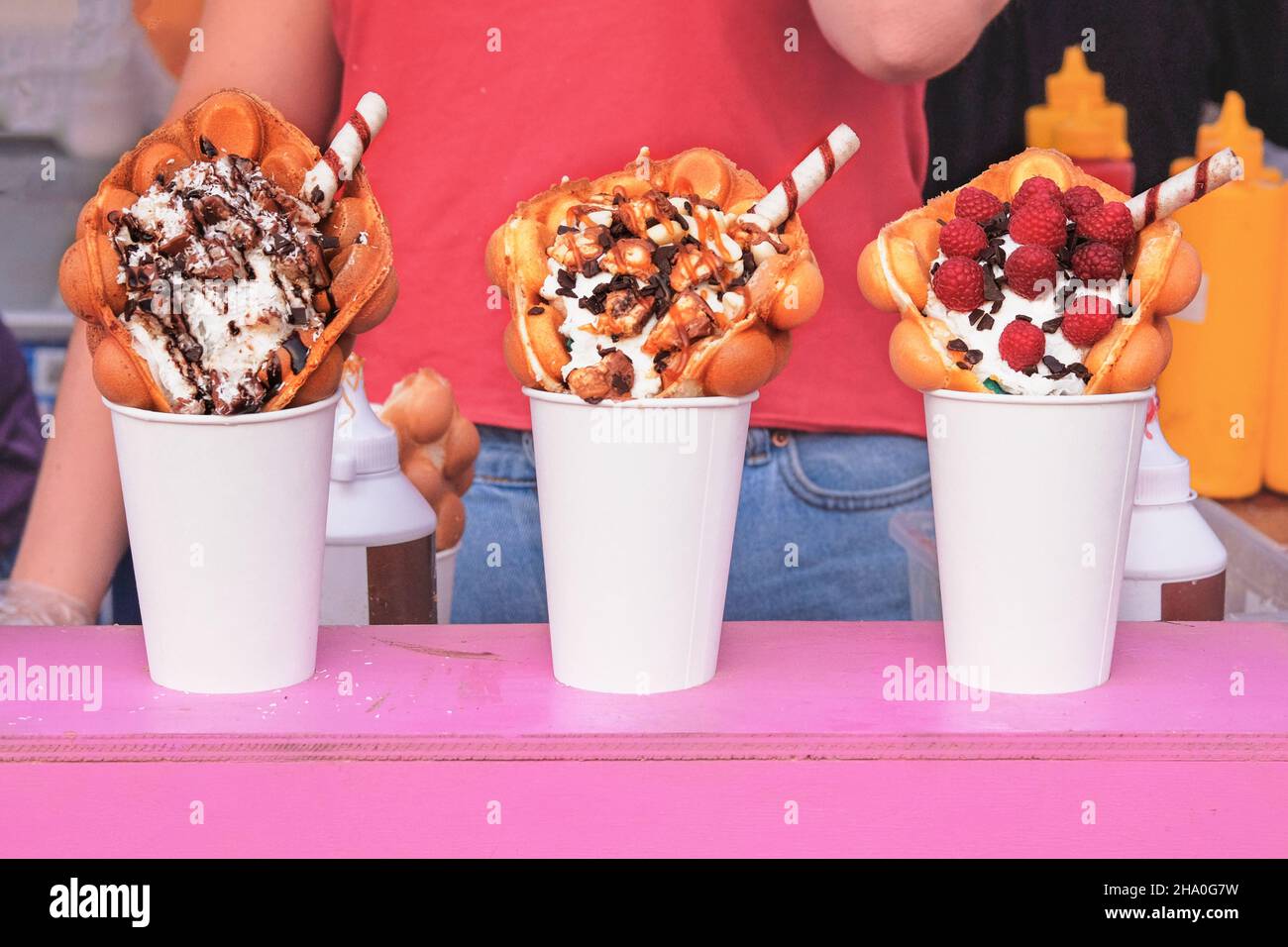 I waffle a bolle d'aria con lamponi, cioccolato e marshmallow in tazze di carta bianca sono venduti durante l'evento del festival del cibo. Cibo dolce di strada in bancarella di cibo. Foto Stock