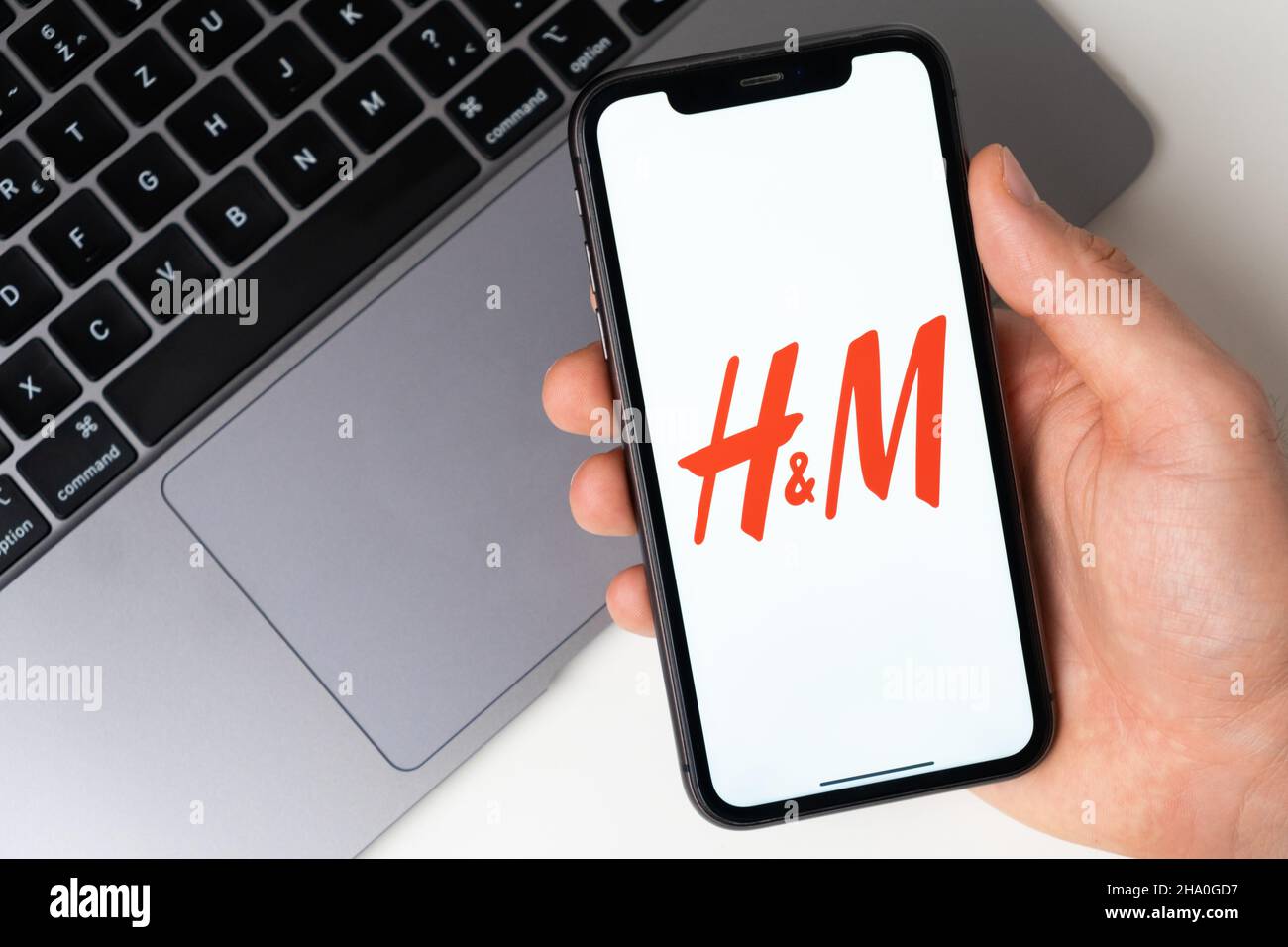 Logo dell'app H e M sullo schermo dell'iPhone per lo shopping online con un laptop sullo sfondo. Novembre 2021, San Francisco, USA Foto Stock